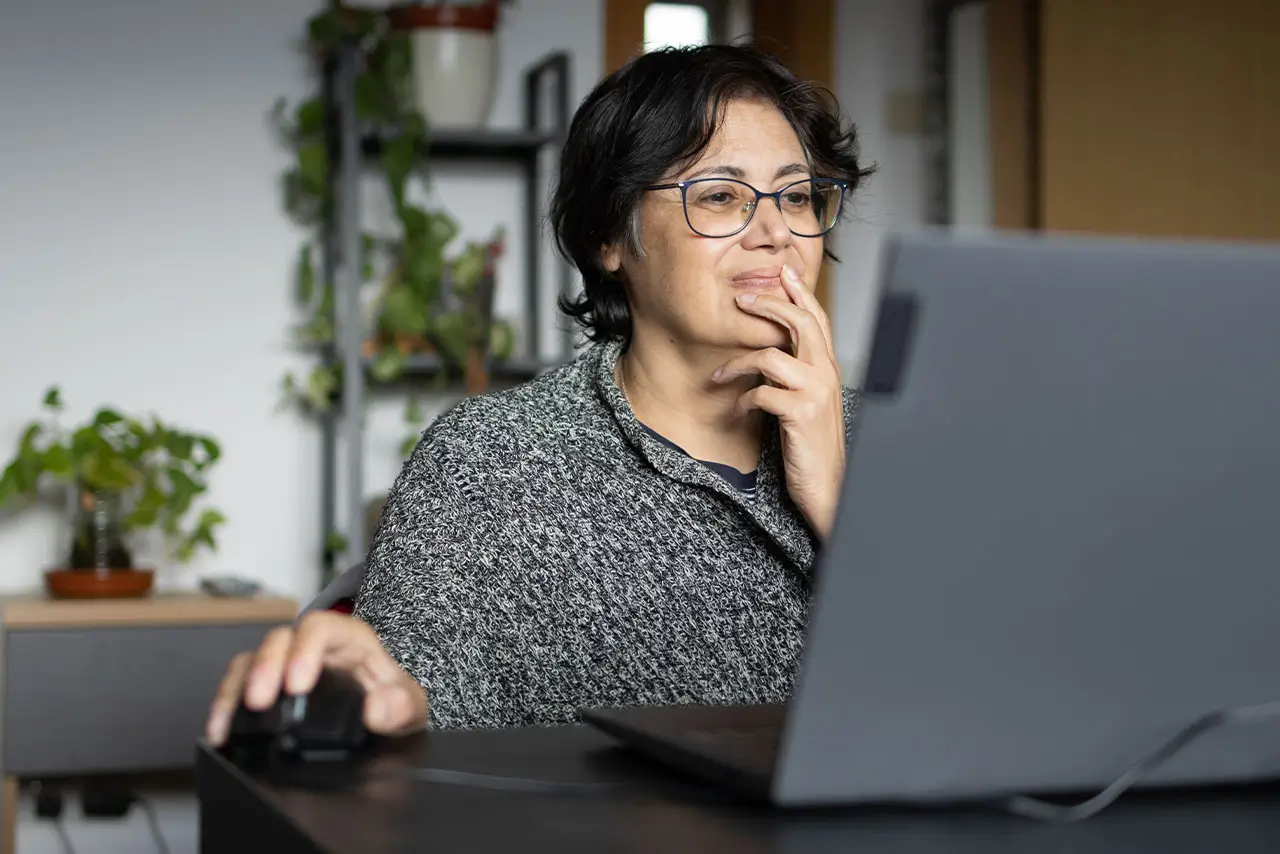 An adult student smiles while working on their laptop in a home office.