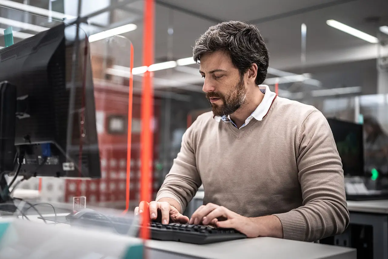 A person working on their computer while seated in an office cubical.