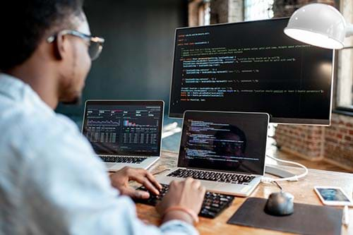 person looking at code on three computer screens