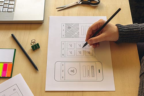 person with a pencil drawing out a mock-up of a phone app